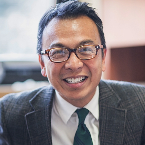 Eduardo Capulong smiles in a suit and glasses