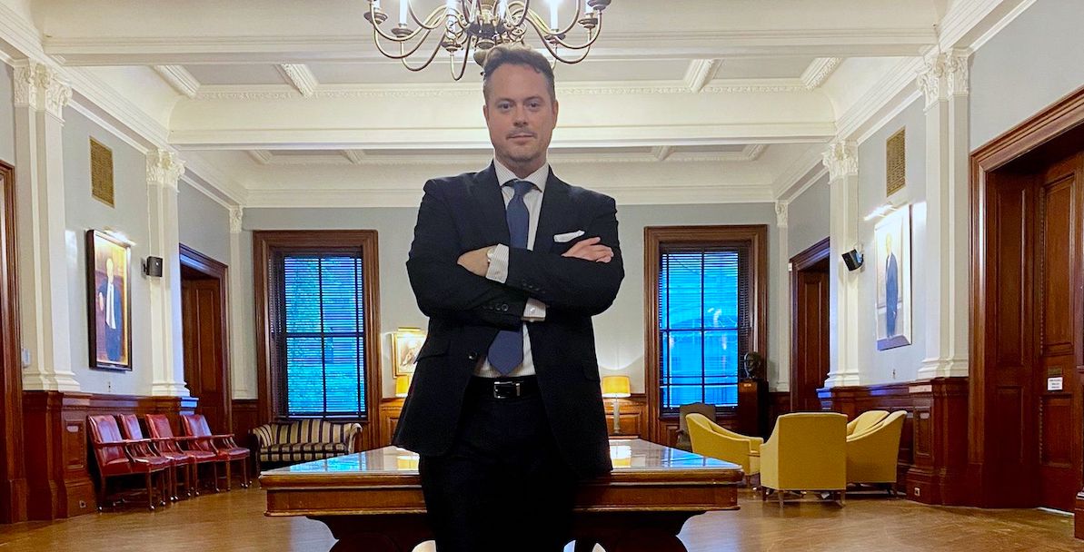 Jason Moor stands in a suit, arms folded, in a room