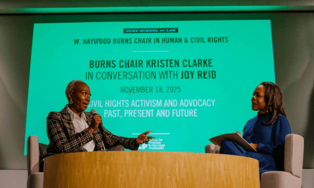 Two women sit on stage engaging in a discussion. The background screen reads: