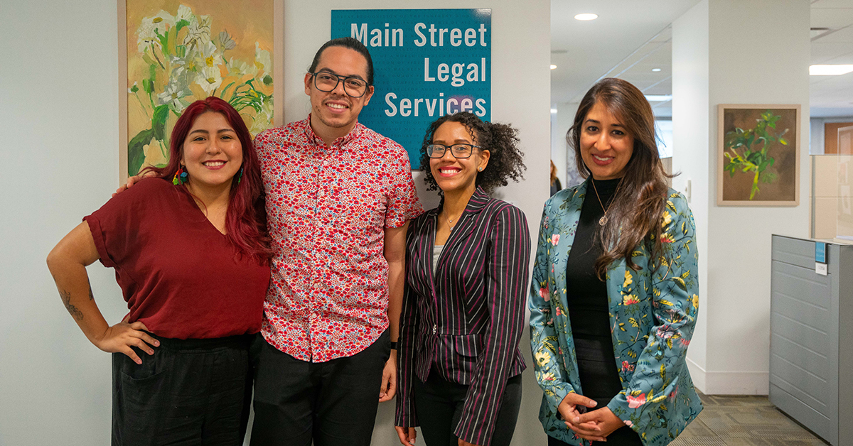 Students, Jazmin Ortiz and Raquel Morote standing with client, Wendell, and Professor Nermeen Arastu in front of Main Street Legal Services sign.
