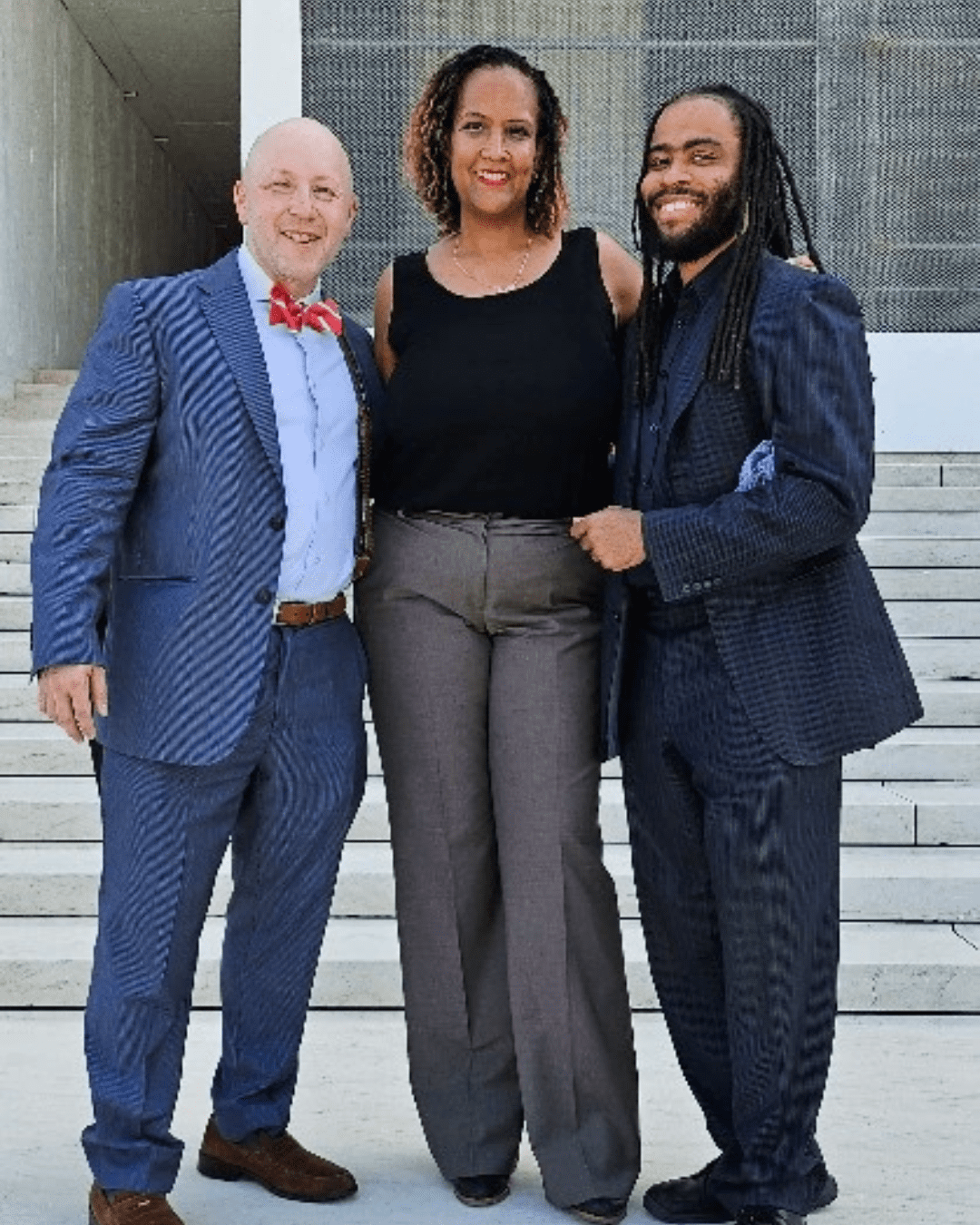 Three people in professional attire standing in front of the steps of the U.S. Supreme Court.