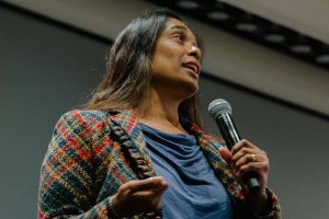 2026-01-16_Pre_Law_Conference_2nd_Annual (11 of 33) Close-up of Sudha Setty holding a microphone while speaking on stage, captured from a low angle with stage lighting visible overhead.