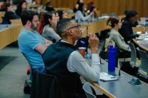 2026-01-16_Pre_Law_Conference_2nd_Annual (15 of 33) An audience member sits in a lecture hall at CUNY School of Law, holding a pen and listening attentively during a conference session, with other attendees seated nearby.