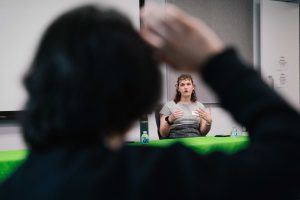 2026-01-16_Pre_Law_Conference_2nd_Annual (17 of 33) A panelist speaks from behind a table covered with a green CUNY School of Law tablecloth, gesturing while addressing attendees seated in the foreground.
