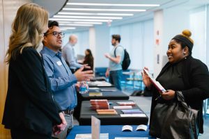 2026-01-16_Pre_Law_Conference_2nd_Annual (22 of 33) Two representatives and an attendee converse at an informational table displaying brochures and books during the pre-law conference.