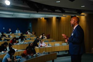 2026-01-16_Pre_Law_Conference_2nd_Annual (9 of 33) A speaker in a suit addresses a seated audience in a lecture hall at CUNY School of Law, gesturing while speaking from the front of the room.