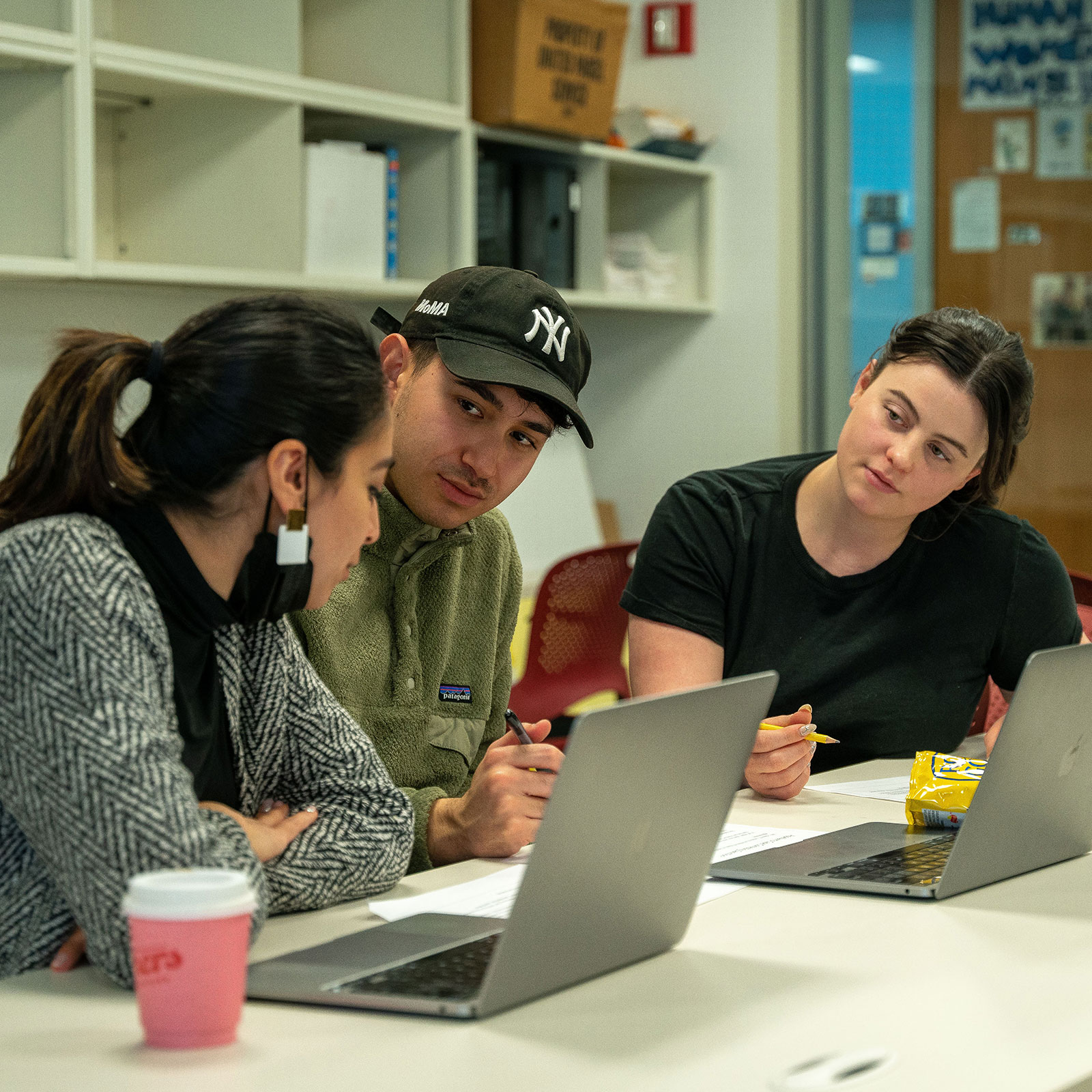 Three students sitting at table with laptops reviewing class work.