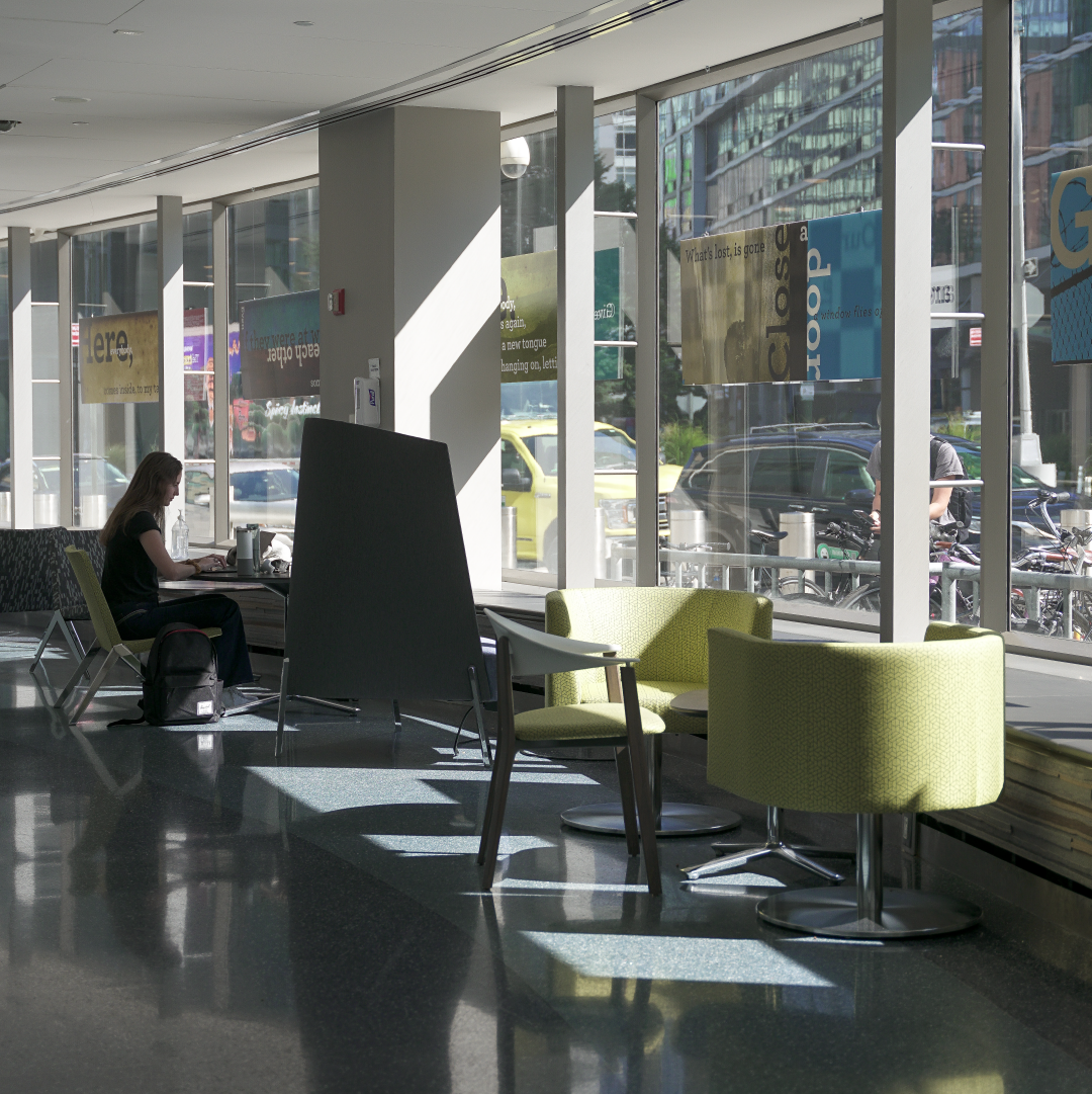 a person sits working at at table in front of a large window at CUNY Law