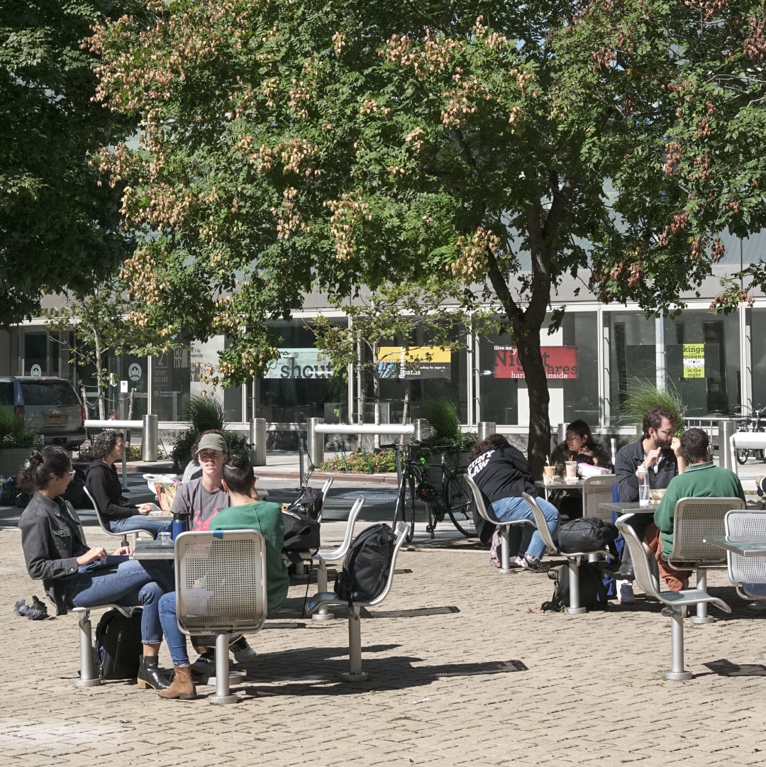 Students, faculty & staff sitting reading, studying or eating lunch, out in the triangle park across from the CUNY School of Law campus building,