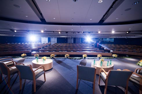 From the backstage wing, a view of the the stage with coffee tables and chairs and the seats in the audience.