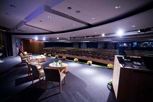 From the backstage, a view of the the stage with coffee tables and chairs and the seats in the audience.