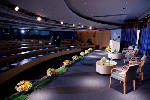 From the backstage wing, a view of the the stage with coffee tables and chairs and the seats in the audience.