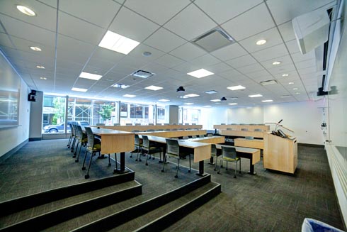 Auditorium tiered style classroom with podium on bottom center row with white board and digital screen