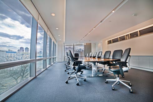A conference room with a one wall of windows and a very large table in the center with at least 12 office chairs