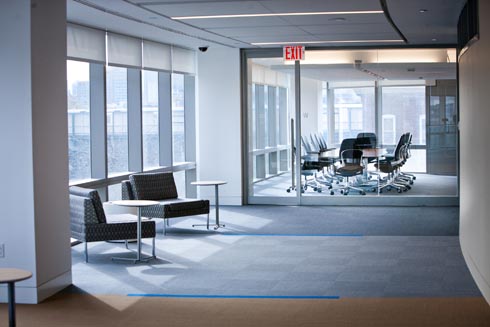 View of large corner windowed conference room with a very large table in the center with at least 12 office chairs and the AV technology necessary for presentations and virtual meetings