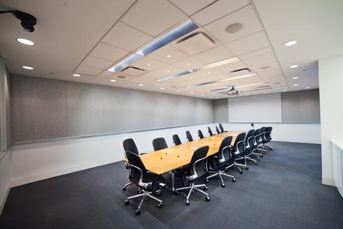 A conference room with a very large table in the center with at least 12 office chairs and the AV technology necessary for presentations and virtual meetings