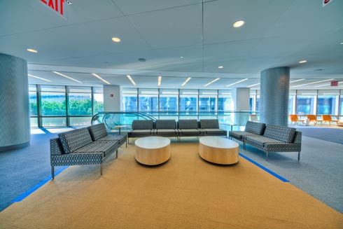 Very large hallway with one wall lined with windows and a large space for people to gather on sofas with round coffee tables