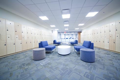 Very large hallway with walls lined with lockers and a large space for people to gather on sofas with round coffee tables