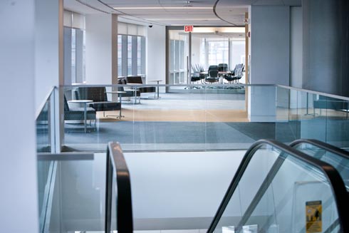 View from the top of the third floor escalator of the hall lined with study seating sections along the curved wall of windows