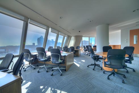 Seating and study areas by a curved wall of windows overlooking a view of Queens and the City