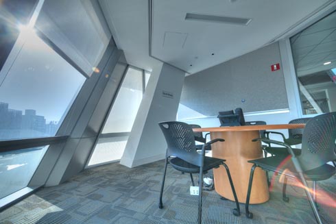 Seating and study areas by a curved wall of windows overlooking a view of Queens and the City