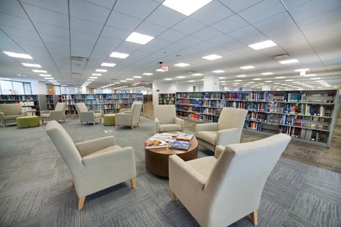 Comfy reading chairs with tables arranged near the book stacks in the library.