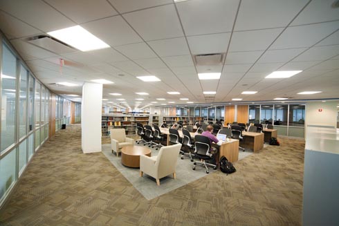 Comfy reading chairs with tables arranged near the book stacks and study tables in the library.