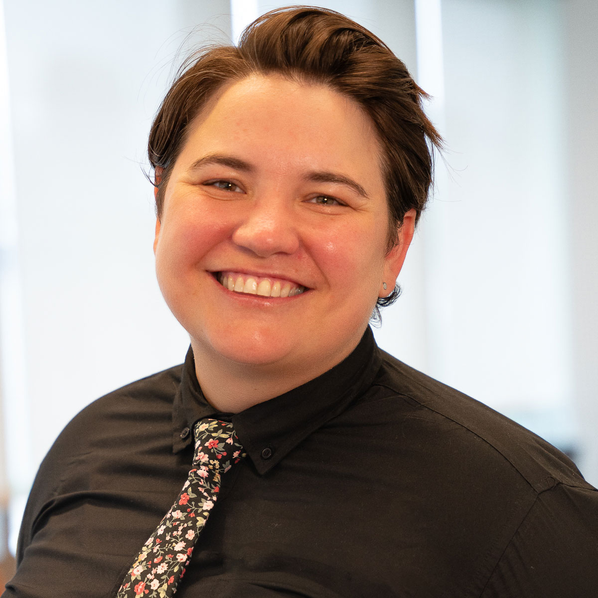 Kara, dressed in a black button-down and floral tie smiles.