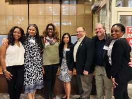 a group of seven people posed together facing the camera and smiling Busboys and Poets at the Alumni Happy Hour in DC.