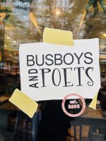 The front door of Busboys and Poets. The decal looks like a white post it note with three strips of beige masking tape. The letters on the white post it note say "Busboys and Poets"