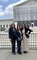 Three people stand in front of the U.S. Supreme Court. The exterior of the Court is partially obscured by scaffolding.