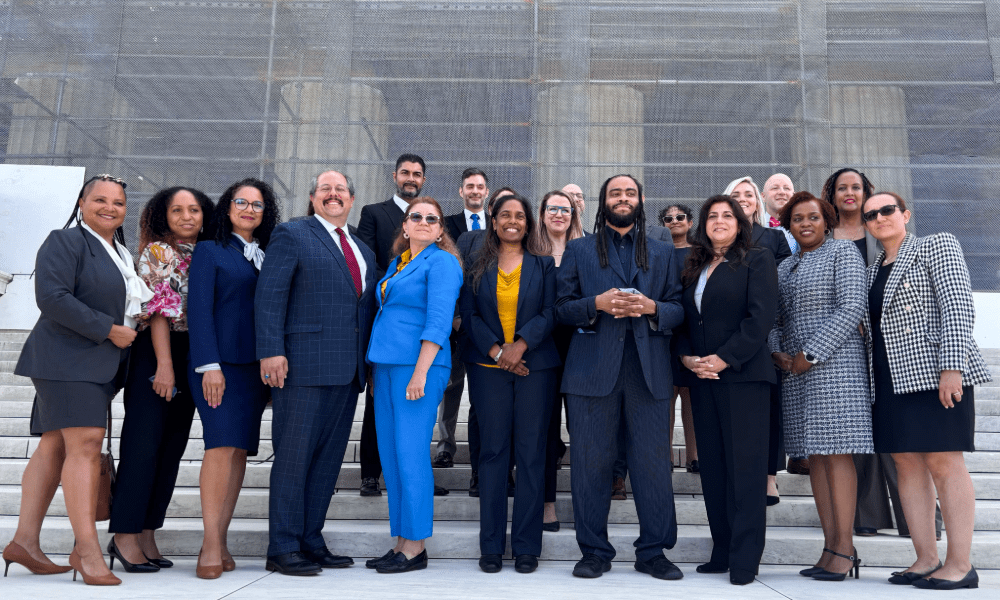 A group of over 20 CUNY Law alums in professional attire standing on the steps in front for the U.S. Supreme Court.