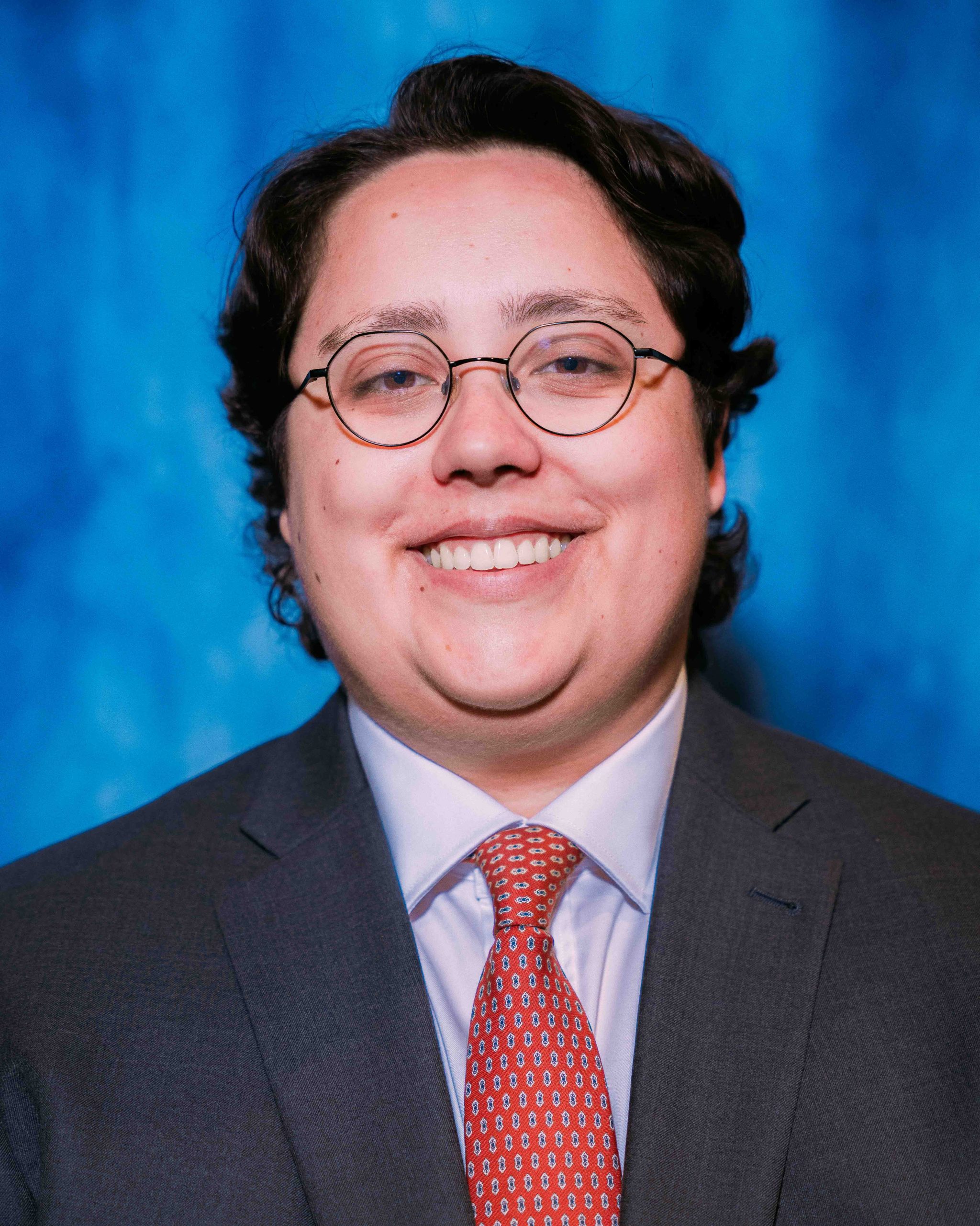 Amy Villanueva poses for a Graduate portrait in a gray business suit with red decorative necktie.