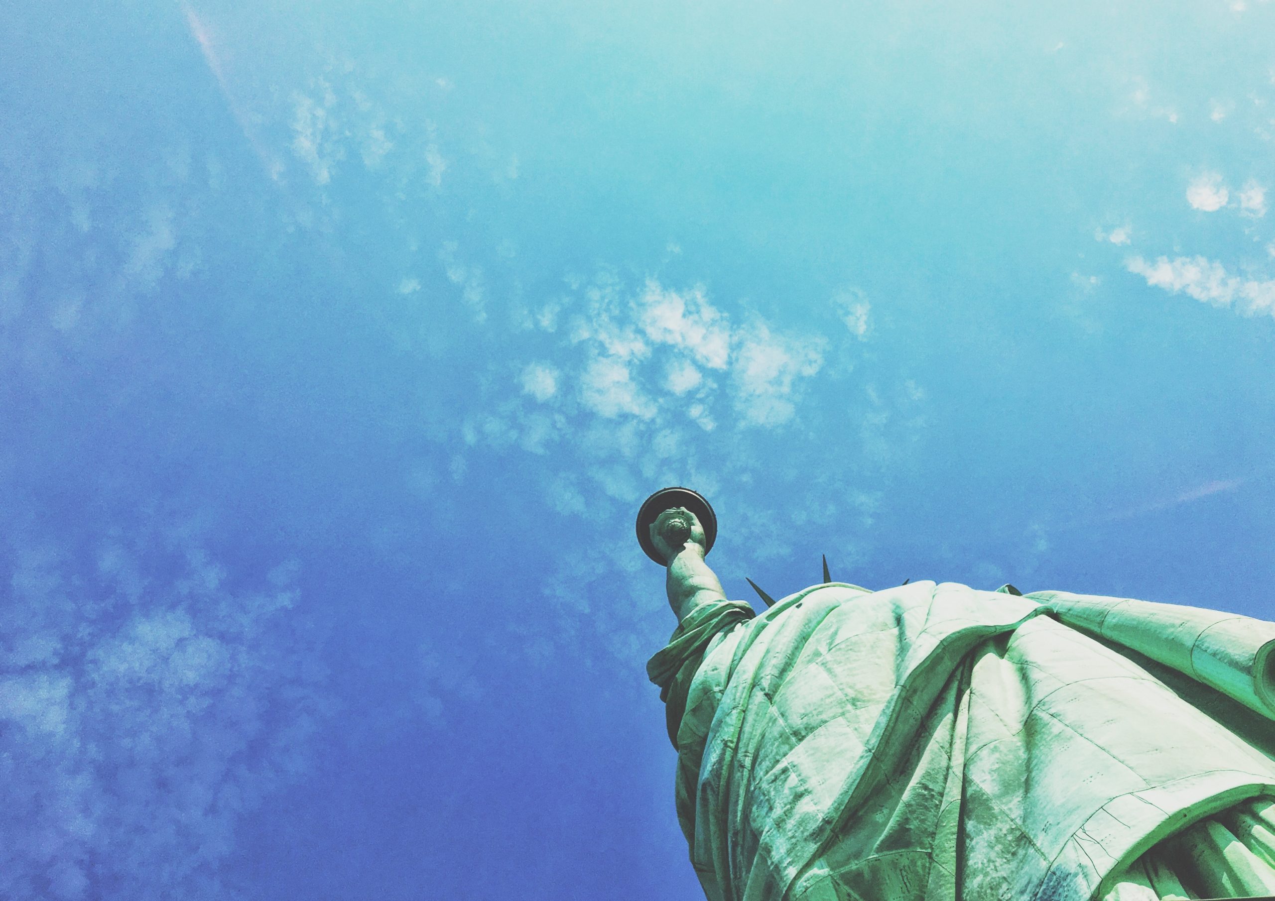 A view looking up at the Statue of Liberty against blue sky