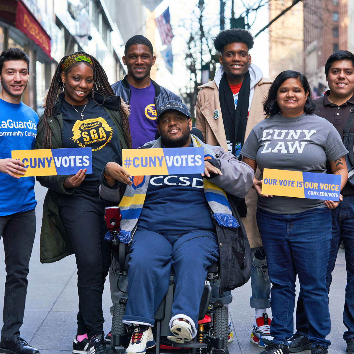 Students gathered around outside holding signs #CUNYVotes #OurVoteIsOurVoice