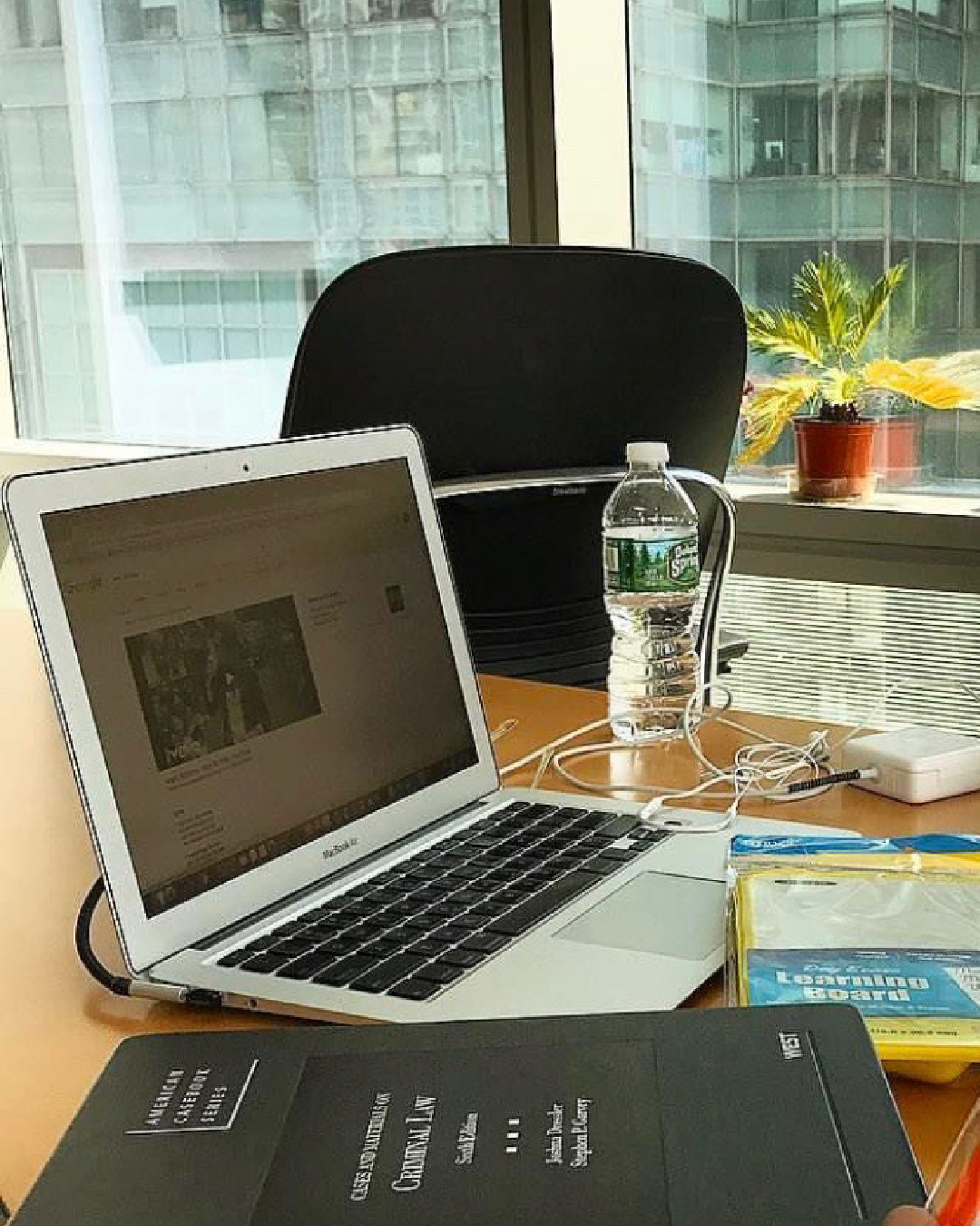 A laptop next to law books on a a table in the CUNY Law library next to the window.